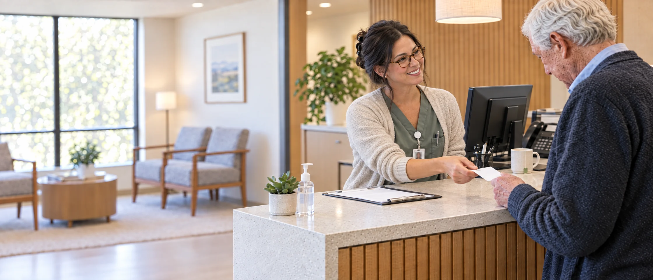 A front-desk coordinator in glasses handing an older patient his appointment card